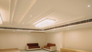 A spacious room with a high ceiling, recessed lighting, and a chandelier. There are two sofas and a table with a draped tablecloth.