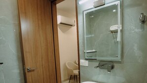 A modern bathroom with a wooden door, a white sink, a mirror, and a shower area. - The Camellia Grand  (Lucknow)