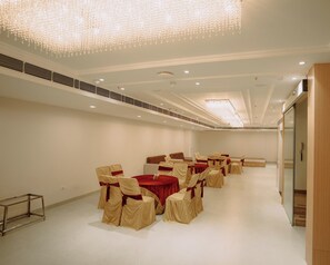 A spacious banquet hall with rows of tables and chairs, a chandelier, and a modern ceiling design. - The Camellia Grand  (Lucknow)