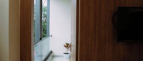 A hallway with a wooden door leading to a balcony with potted plants.
