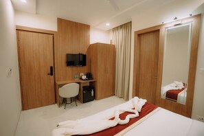 A hotel room with a bed, a desk with a chair, a television, and a wardrobe. - The Camellia Grand  (Lucknow)