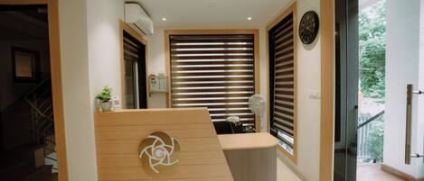 A reception area with a wooden reception desk, a wall-mounted clock, and a window with blinds.
