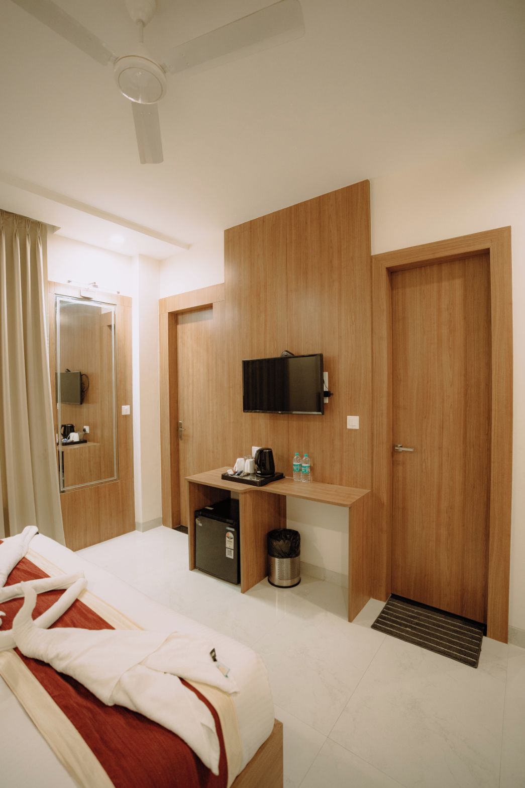 A hotel room with a bed, a desk with a television, a mirror, and a shower area.