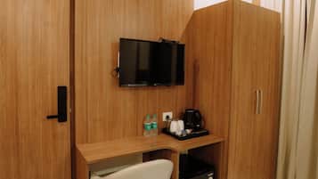 A hotel room with a wooden wardrobe, a desk with a chair, a television, a mini-fridge, and a coffee maker.
