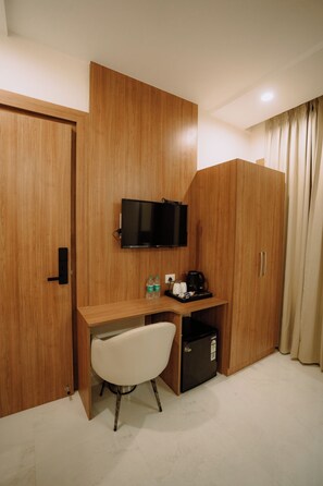 A hotel room with a wooden wardrobe, a desk with a chair, a television, a mini-fridge, and a coffee maker. - The Camellia Grand  (Lucknow)