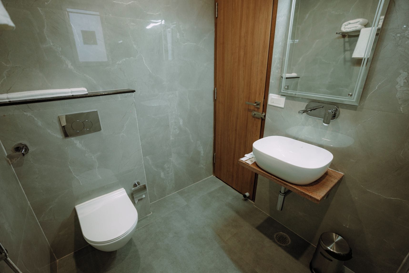 A modern bathroom with a toilet, a sink, a shower, and a wooden door.