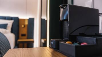A hotel room with a bed, a wooden nightstand, a black coffee machine, and a black storage box.