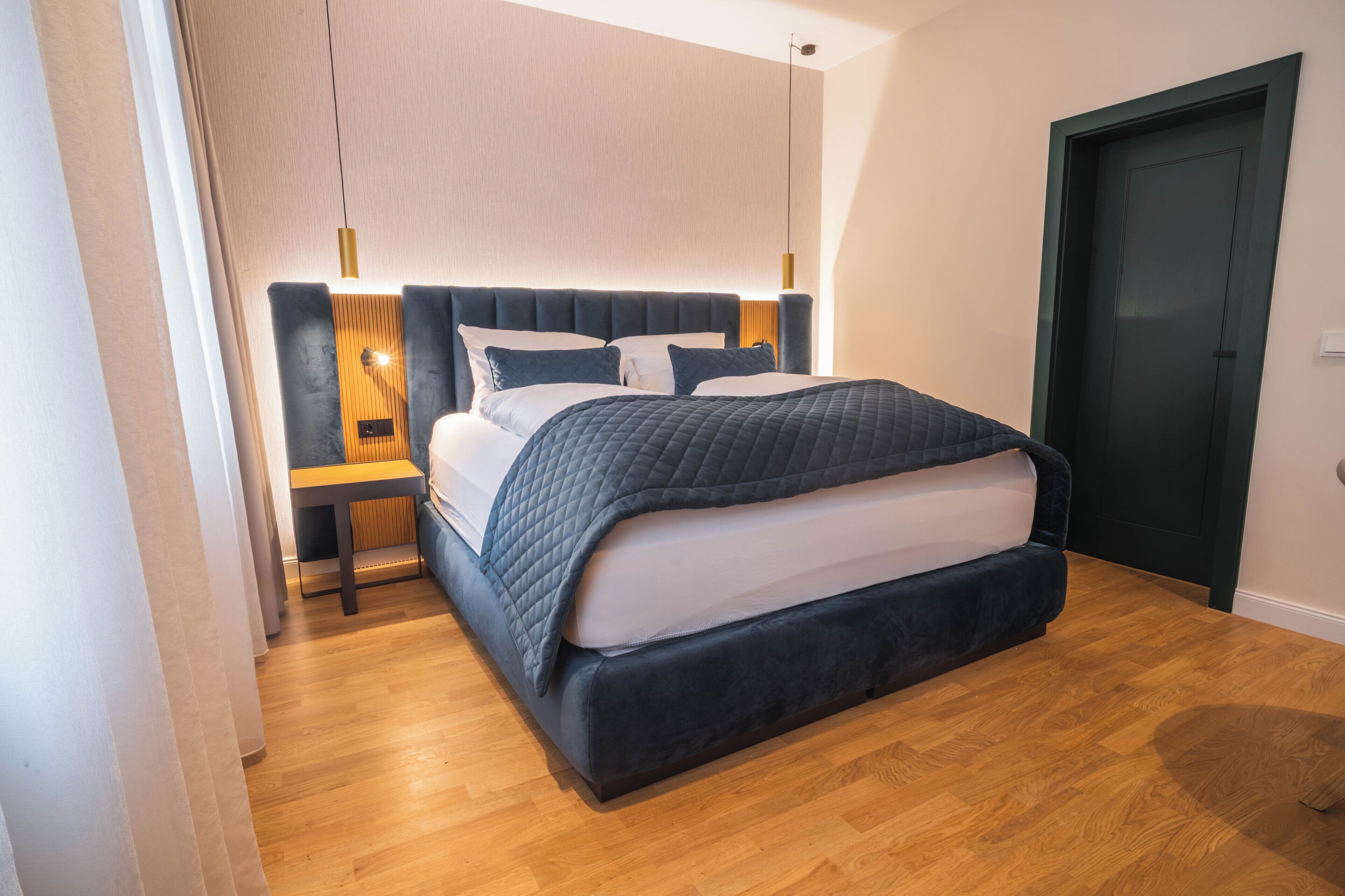 Quarto moderno com uma cama grande, mesas de cabeceira e uma porta de cor escura.