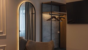 Quarto de hotel com uma cama, uma cadeira, um guarda-roupa com espelho e uma televisão na parede.