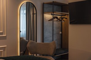 Habitación de hotel con cama, una silla, armario con espejo y televisor montado en la pared.