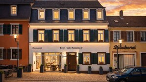 Hotel com restaurante no andar térreo, várias janelas com persianas e rua de calçada.