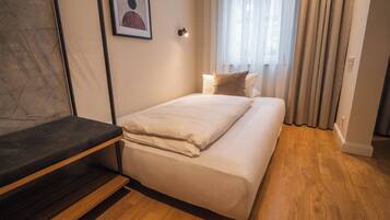 Un dormitorio con cama, una banca, una lámpara de pared y un ventanal con cortinas.