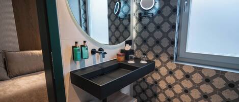 Un baño moderno con un lavabo negro, dos espejos, un perchero para toallas y baldosas estampadas.