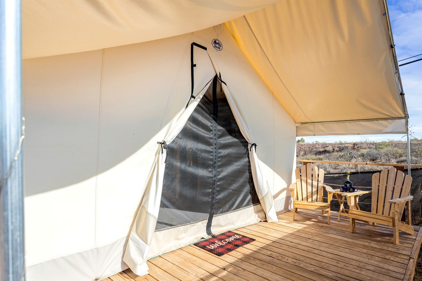 Una carpa con interior negro, un felpudo y sillas de madera en una terraza.