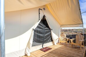 Een tent met een donker interieur, een voetmat en houten stoelen op een terras.