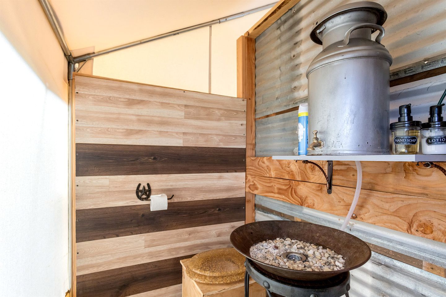 A compact bathroom with a wooden vanity, a metal sink, and a storage shelf with toiletries.