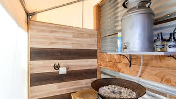 A compact bathroom with a wooden vanity, a metal sink, and a storage shelf with toiletries.