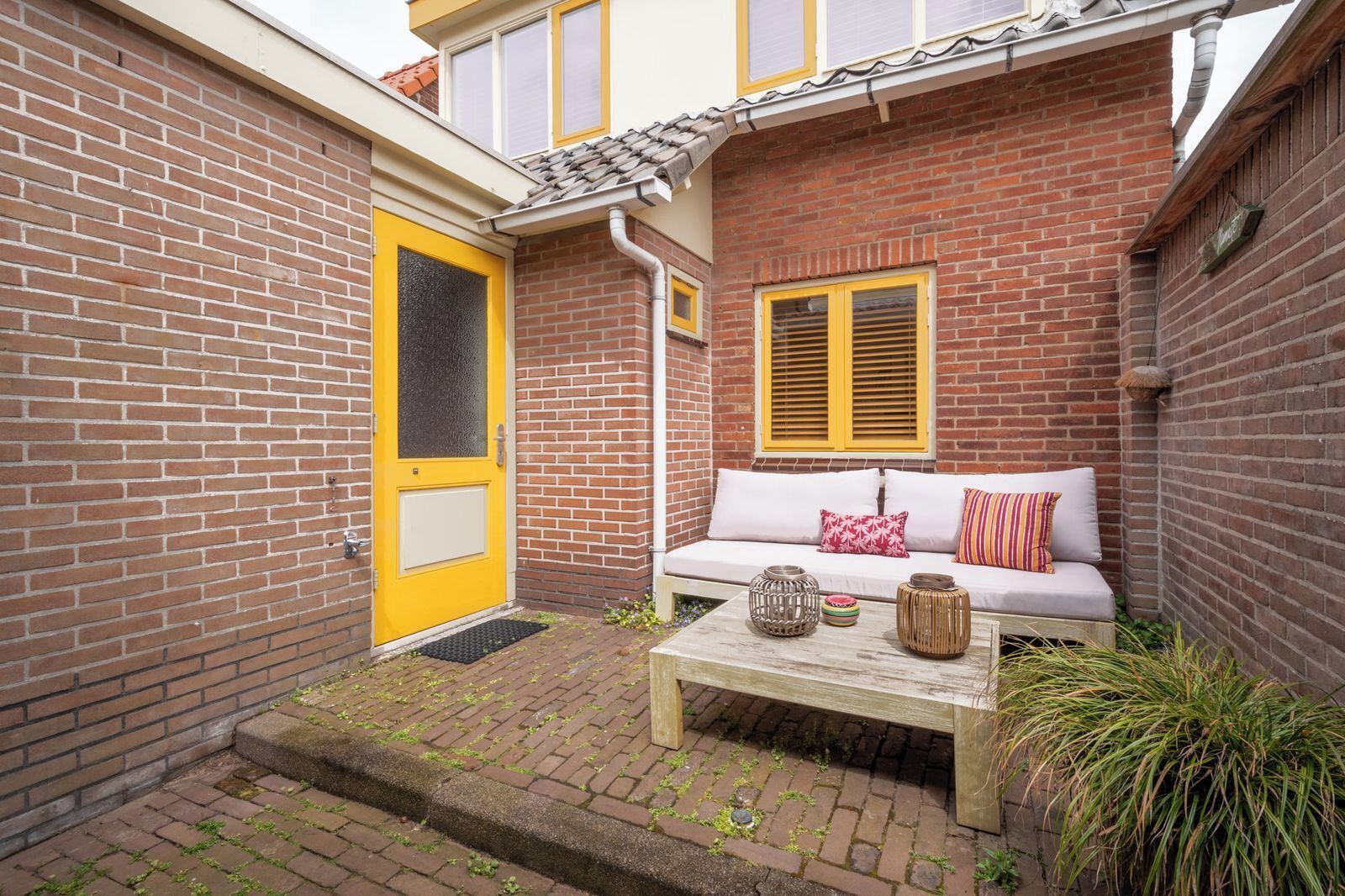 A brick building with a yellow door, a white sofa with cushions, and a wooden table with decorative items.
