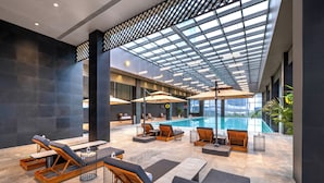A modern indoor pool area with lounge chairs and umbrellas, a pool, and a glass ceiling. - International Hotel LuoYang (Luoyang)