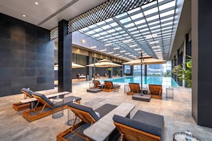 Un área de piscina interior moderna con sillones de descanso y sombrillas, piscina y techo de cristal.