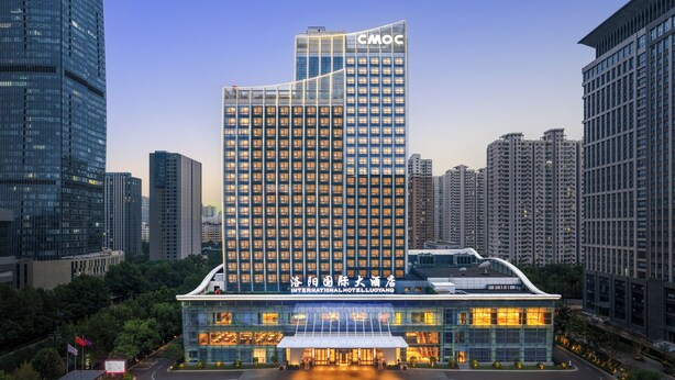 Un hotel moderno con un destacado edificio CMOC al fondo, que cuenta con un amplio muro de cristal y una terraza en la azotea.