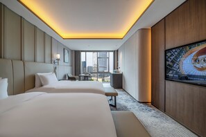 Habitación de hotel con dos camas, televisor y vista a la ciudad.