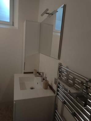 Un baño con lavamanos blanco, espejo, dispensador de toallas y zona de ducha.