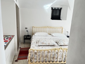 Un dormitorio con una cama, una mesita de noche, una ventana pequeña y una alfombra roja.