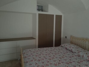 Un dormitorio con cama, armario y una ventana pequeña.