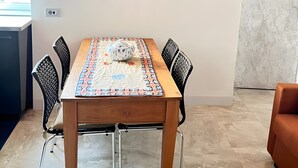 A dining area with a wooden table, black chairs, and a patterned tablecloth. There are two framed pictures on the wall, and a QR code is visible. - 'Crooked House' Apartment with Mountain View, Private Garden and Parking (Naggio)