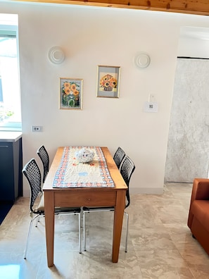 Comedor con mesa de madera, sillas negras y mantel estampado. Se observan dos cuadros en la pared y un código QR.