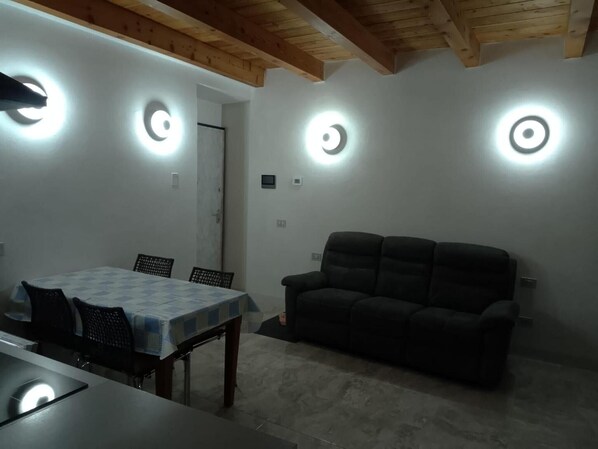Un comedor con una mesa y sillas, un sofá y tres luces fijadas a la pared.