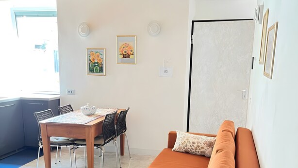 A modern living space with a sofa, a dining table, and chairs. There are wall-mounted light fixtures and framed artwork. - 'Crooked House' Apartment with Mountain View, Private Garden and Parking (Naggio)