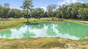 A tranquil outdoor setting with a large green pond, picnic tables, and cabins in the background.