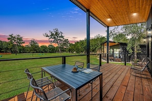 Une terrasse en bois avec une table et des chaises, donnant sur une pelouse et des arbres.