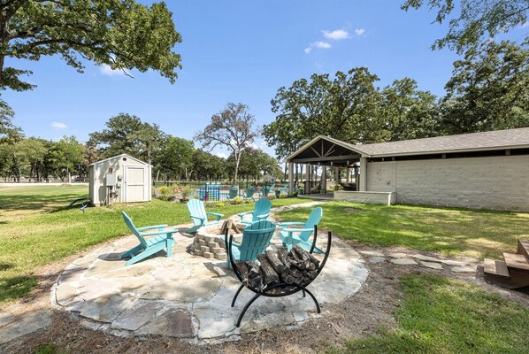 A patio area with Adirondack chairs, a fire pit, and a small shed.