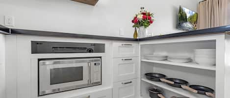 A kitchen with a built-in microwave, white cabinets, a shelf with dishes, and a vase with flowers.