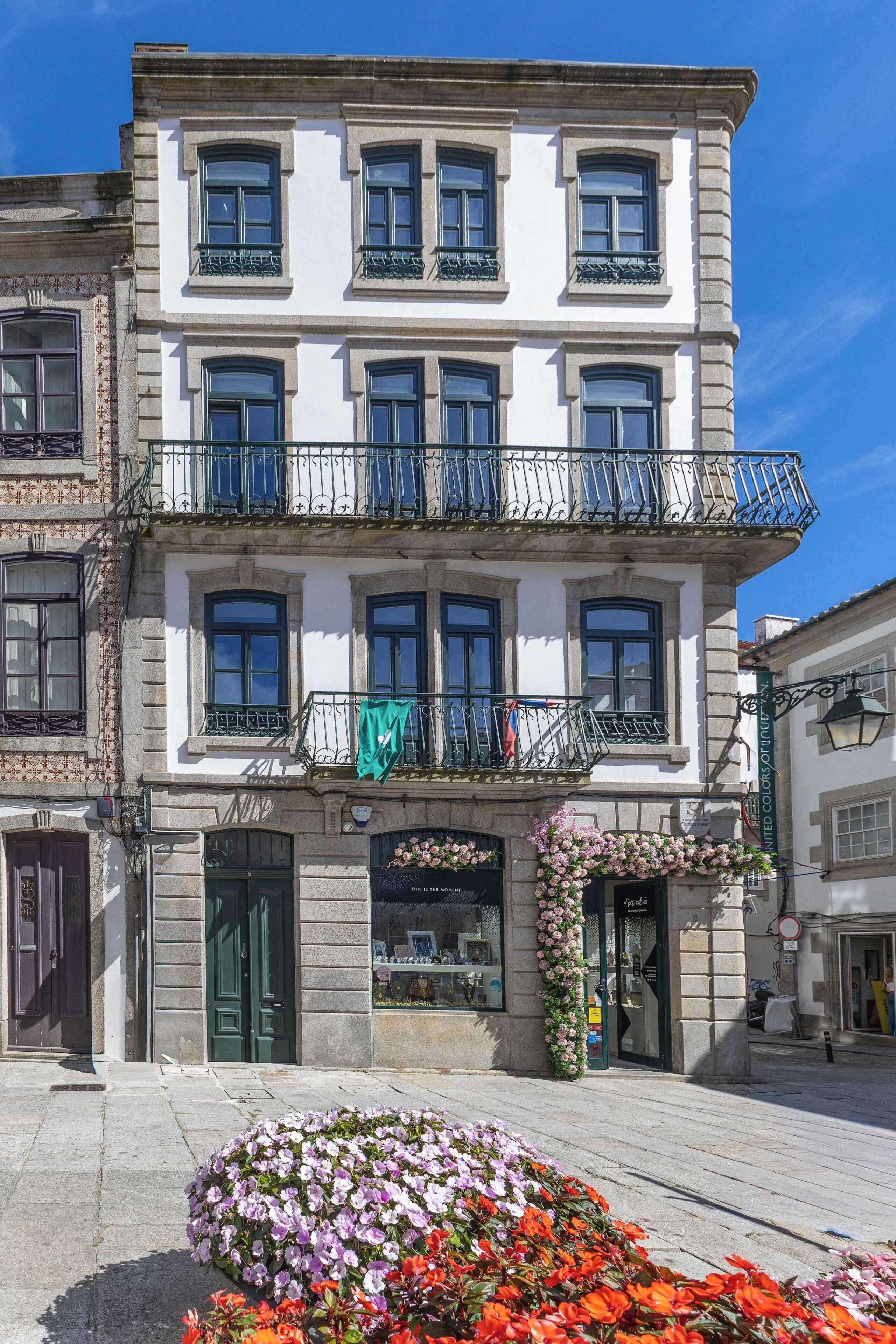 A multi-story building with balconies, a green door, and a flower display.