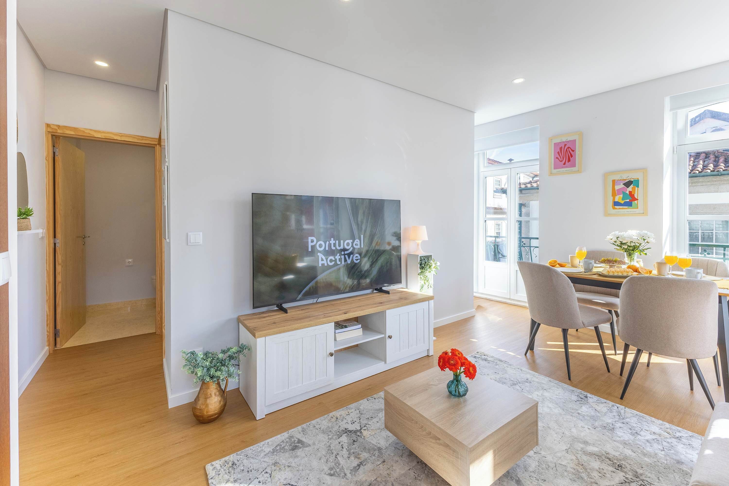 A modern living room with a TV, dining area, and a hallway.
