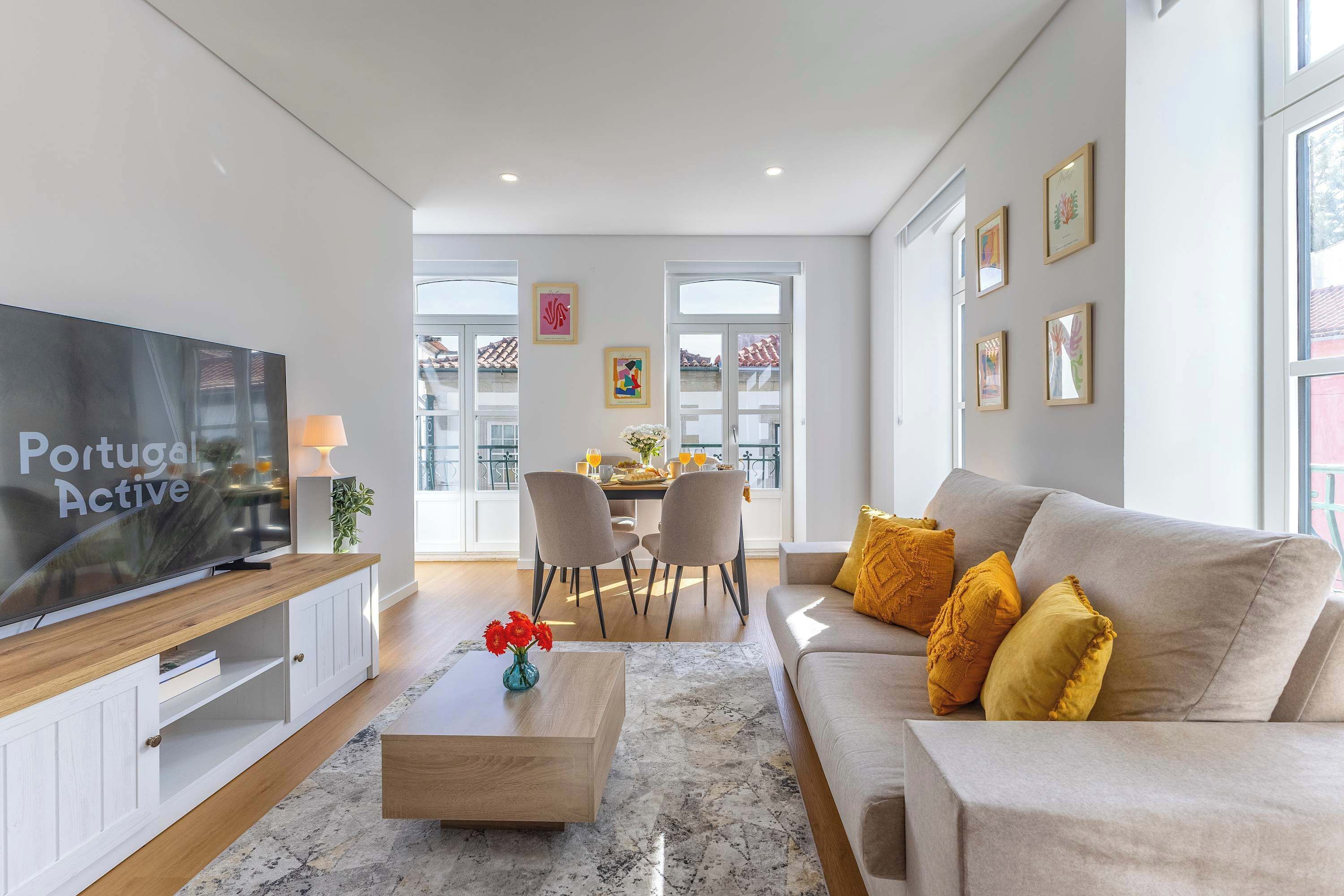A modern living room with a flat-screen TV, a sofa, a coffee table, and a dining area in the background.