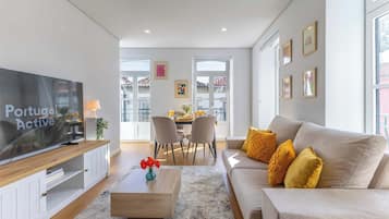 A modern living room with a flat-screen TV, a sofa, a coffee table, and a dining area in the background.