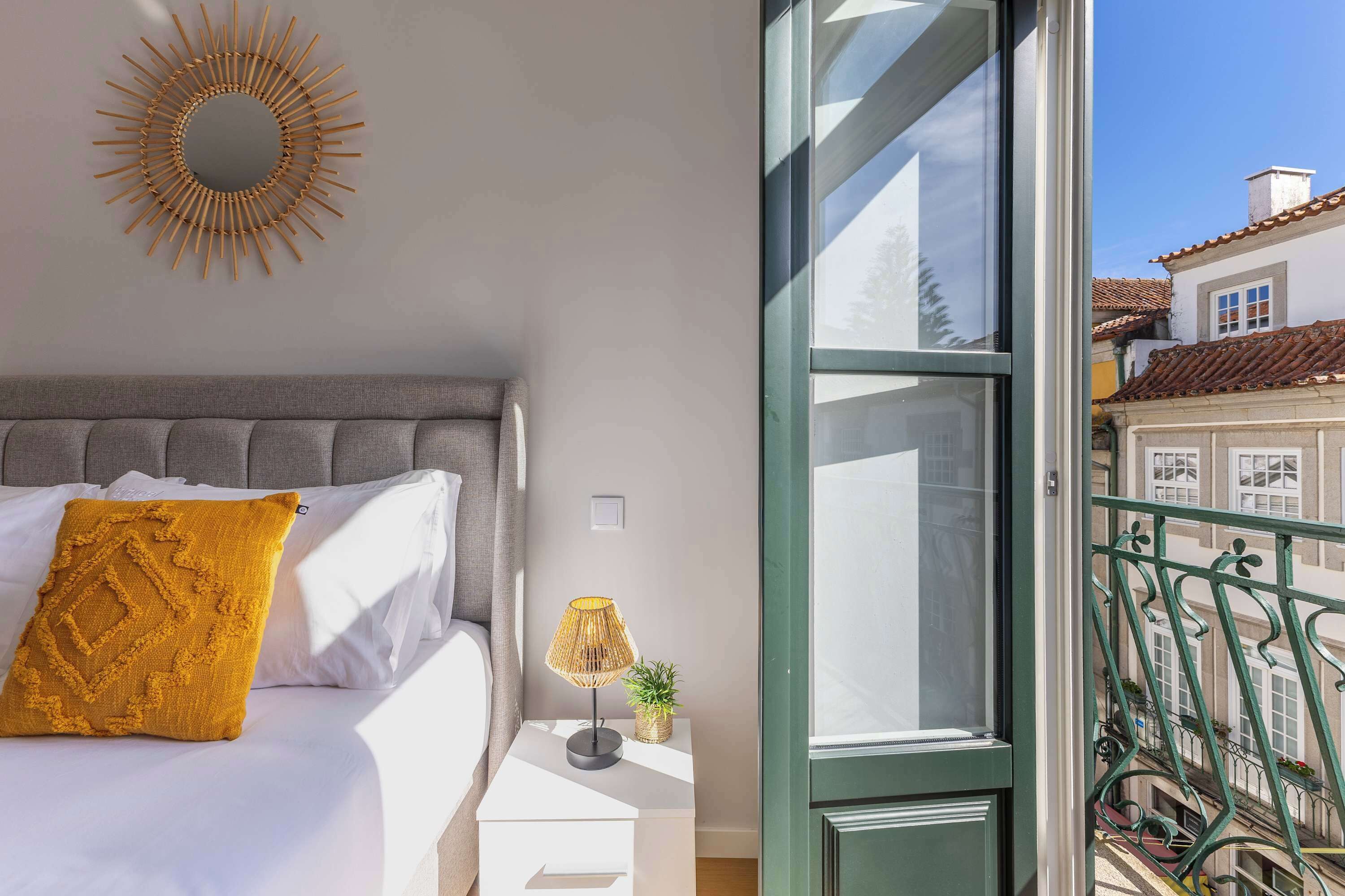 A bedroom with a bed, a bedside lamp, a mirror, and a view of a balcony.