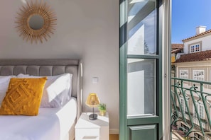 Una camera da letto con un letto, una lampada da comodino, uno specchio e vista su un balcone.
