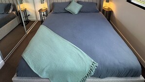 Une chambre à coucher avec un lit, un grand miroir, un tableau encadré au mur et des lampes de chevet.