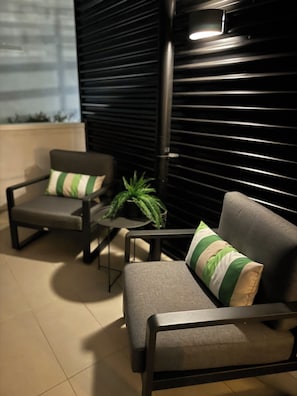 A seating area with two chairs and a small table, a potted plant, and a black shuttered wall.