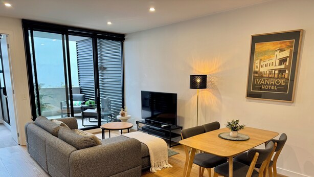 Un salon moderne avec un canapé, un téléviseur, une table à manger et un balcon offrant une vue agréable.