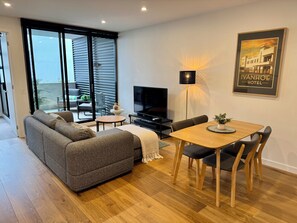 Una sala de estar moderna con sofá, televisor, mesa de comedor y un balcón con vistas.