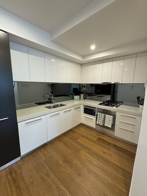 A modern kitchen with white cabinets, a stainless steel sink, and a wooden floor.