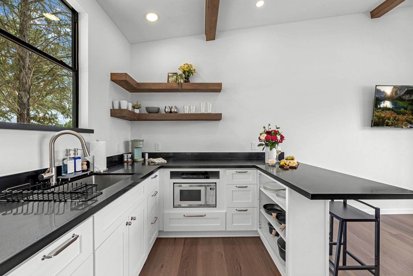 Una cocina moderna con armarios blancos, encimeras negras, horno empotrado y una viga de techo de madera.
