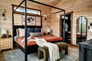 Ein Bett mit Baldachin, ausgestattet mit einer roten Bettdecke, einer Bank und einem Nachttisch mit Lampe.